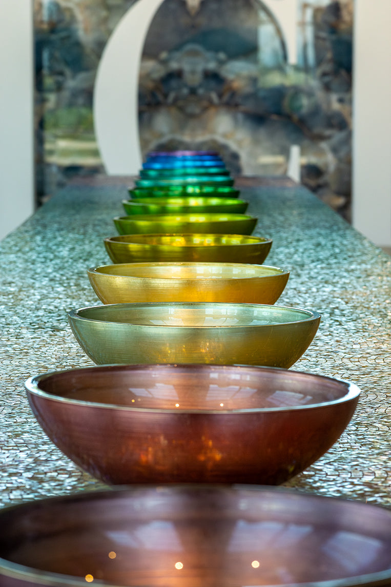 Round glass basins in a row in different green, blue and gold tones.