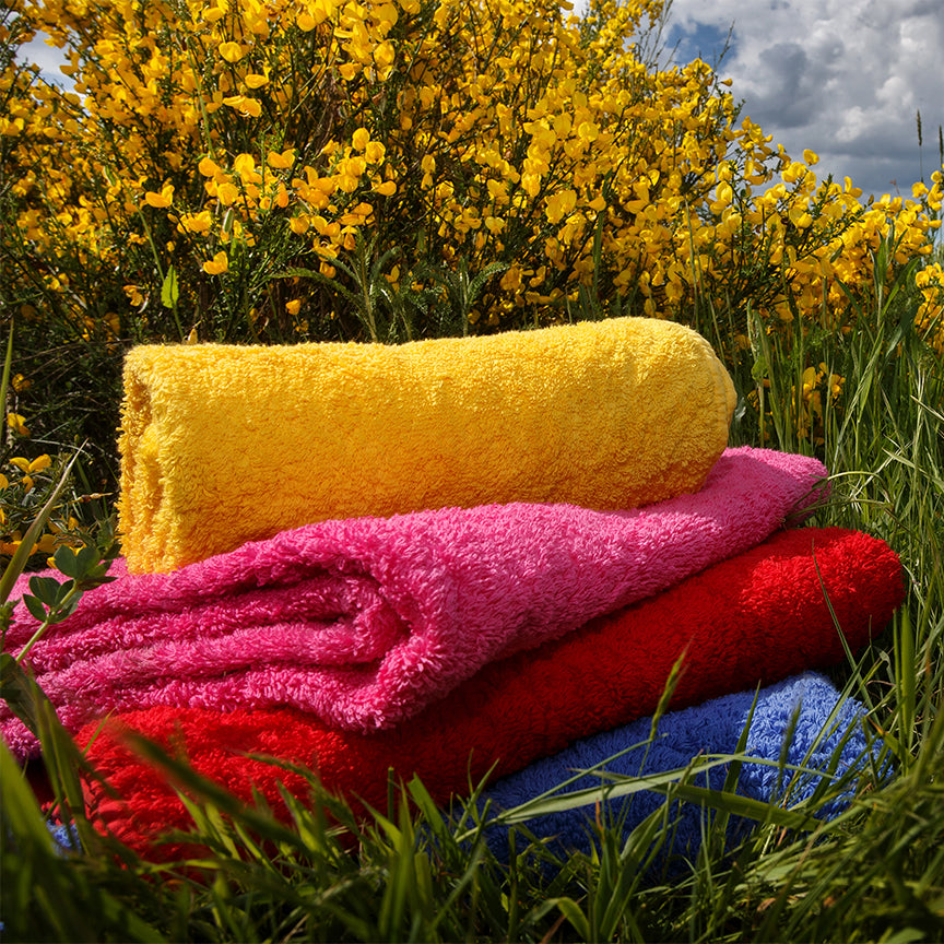 Luxus Handtücher in Gelb, Pink, Rot und Blau, arrangiert im Gras vor blühendem Ginster